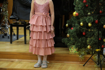 A girl sings a song standing on the stage near a decorated Christmas tree