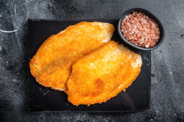 Fried breaded tilapia fillets on a marble board. Black background. Top view