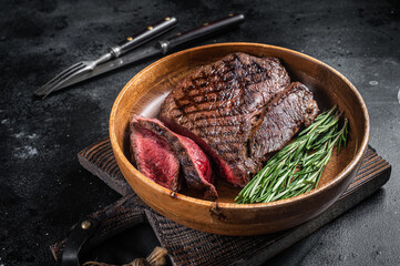 BBQ Grilled Medium Rare top sirloin beef steak, rump steak in a wooden plate. Black background. Top...