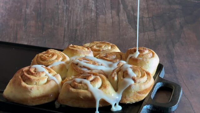 plate of sweet cinnamon rolls with white frosting being pored on them 4k 