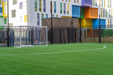 Soccer sports field with green synthetic artificial grass and gate next to a modern school building...