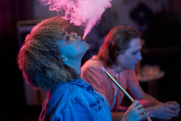 Side view of young Black woman exhaling hookah smoke