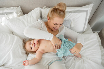 Mother changing clothes or nappy of baby toddler girl on bed at home. Child care, healthy lifestyle, domestic life routine, maternity leave difficulties. Copy space. Top view