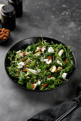 Diet salad with green arugula, feta cheese and pears, almond nuts. Delicacy fresh Green fruit salad on dark background.