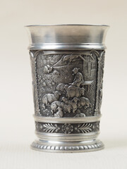 Traditional German vintage pewter wine glass with a bas-relief depicting a shepherd sitting on a bench smoking a pipe and grazing sheep - 556173546