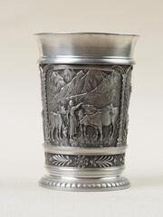 Traditional German vintage pewter wine glass with a bas-relief depicting a shepherdess with a herd of cows against the backdrop of mountains - 556173561