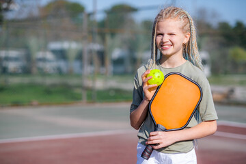 Portrait little teenage girl playing pickleball game, pickleball yellow ball with paddle in hands,...