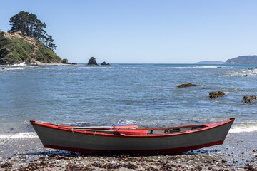 Red and white painted rowing boat at the beach at Isla Maiquillahue in the Pacific Ocean of Chile