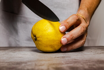 Male hands cutting a ripe yellow lemon with a knife on a slate table. Front view.