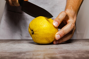 Male hands cutting a ripe yellow lemon with a knife on a slate table. Front view.
