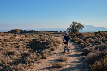 woman cyclist riding a gravel bicycle on the road in hills with mountain view, Alicante region in...