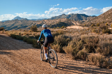 woman cyclist riding a gravel bicycle on the road in hills with mountain view, Alicante region in...