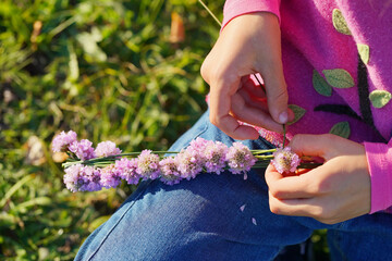 the child's hands weave a wreath of purple flowers