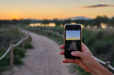 Hand holding phone take a photo beach evening sunset
Woman taking photos of a sunset wit a mobile phone