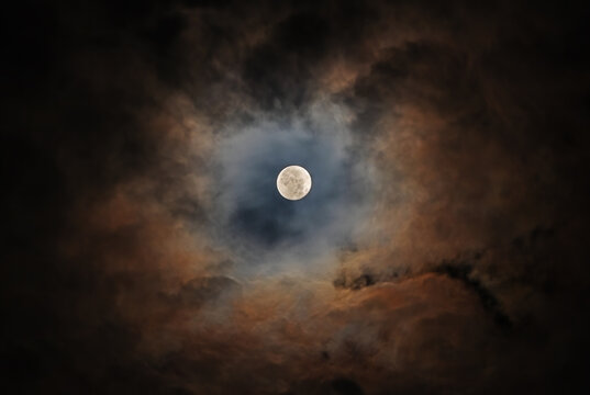The Moon in the night sky is surrounded by beautiful colorful clouds. Photo taken with a telephoto lens