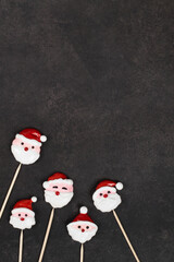 Holiday sweets. Cute Candy in the shape of Santa Claus, covered with colored icing sugar, on a wooden stick. Dark gray background. Top view. Copy space