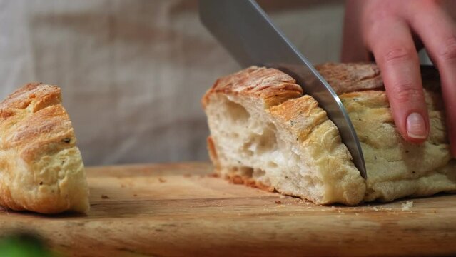 cook slices ciabatta. food cooking, baking and people concept - female baker with knife cutting loaf of bread to slices at bakery or kitchen. Cooking the ciabatta. Italian bread. Baking bread.