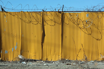 Yellow corrugated metal texture wall with barbed wire in industrial area of the Bronx