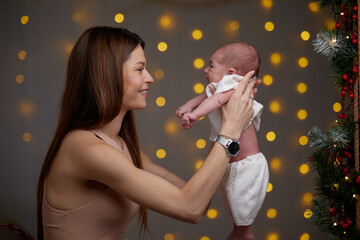 Pretty woman holding a newborn baby in her arms. A woman rejoices, hugs and kisses a child, talks and rejoices her baby, happy smiles on the face of mother and baby.
