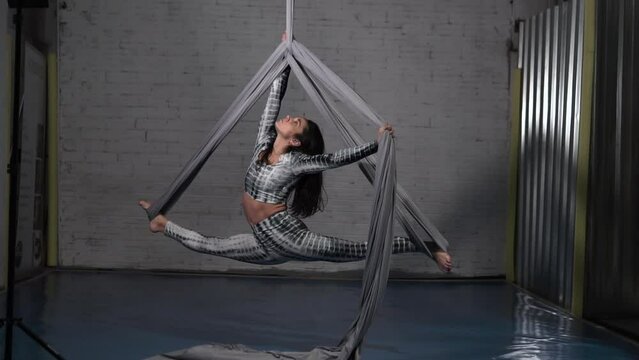 Brunette Acroboat Girl making spectacular split stretch in silk and posing during professional studio shooting
