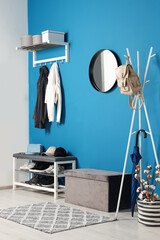Stylish hallway with coat rack and shoe storage bench near blue wall. Interior design