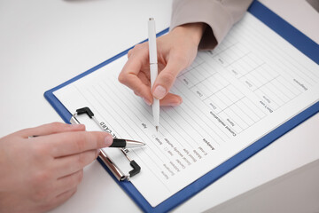 Doctor and patient filling medical card at white table, closeup