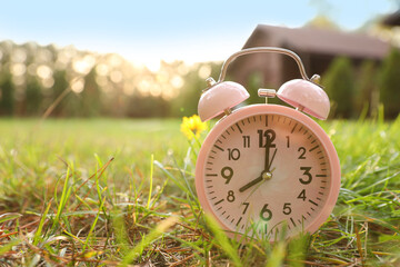 Pink alarm clock on green grass outdoors. Space for text