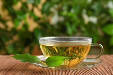 Fresh green tea in glass cup with saucer and leaves on bamboo mat