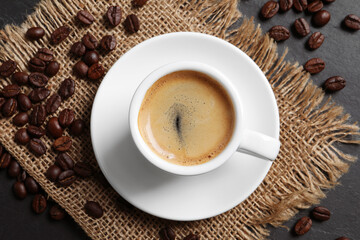 Cup of hot aromatic coffee and roasted beans on black table, flat lay