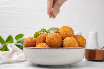 Woman seasoning fried tofu balls with salt at white table, closeup