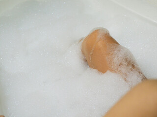 Asian woman legs in a bathtub filled with foam. Relaxation. Body care in bath.