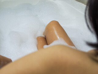 Asian woman legs in a bathtub filled with foam. Relaxation. Body care in bath.