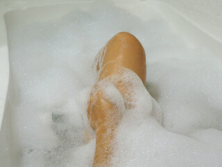 Fototapeta premium Relaxed Asian woman rubbing the skin of her legs with bubbles in the bathtub.