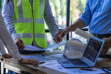 Fototapeta na wymiar Engineer pointing at blueprint and using laptop to draw building design project in office construction concept and meeting structure engineers or architects collaborating with partners.