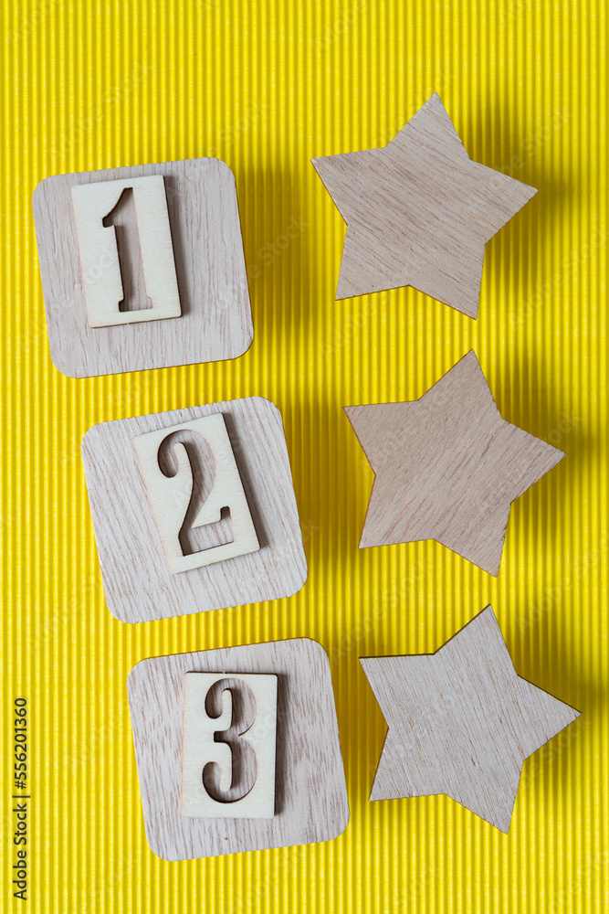 Sticker numbers one, two, three on wood squares near a set of wooden stars on yellow corrugated paper