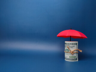 A red umbrella protecting banknotes on a blue background with copy space, planning, saving families, preventing risks and crises, health care and insurance concepts.