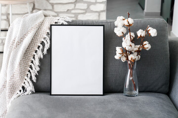 Mock up of black frame with white background. Cotton flowers and empty vertical template on sofa....