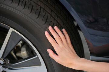 Female driver hands inspecting wheel tire of her new car. Vehicle safety concept