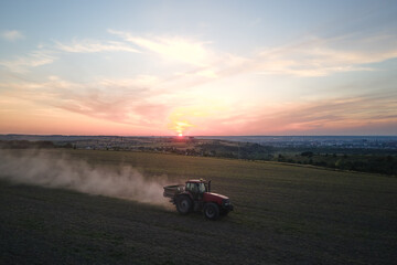 Fototapeta premium Tractor spraying fertilizers with insecticide herbicide chemicals on agricultural field at sunset