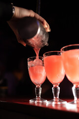Bartender's hand pours a cocktail from a shaker into a long-stemmed glass. Alcoholic cocktails in a nightclub, bar