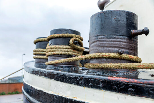Large rusty bollards with coiled ropes on a ship against a gloomy sky. Mooring in the port. Close-up.