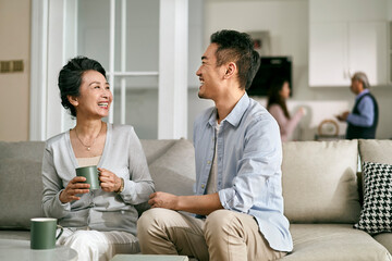 asian elderly mother and visiting adult son chatting at home