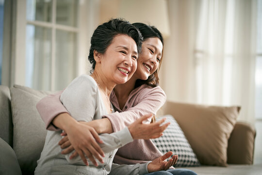 asian adult daughter and senior mother hugging each other at home