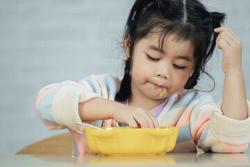 Asian baby girl enjoy happy using cutlery spoon and fork eating delicious noodle in kitchen on...