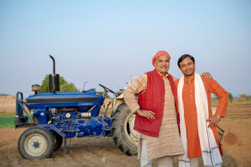 Two Indian farmers standing near tractor at agriculture field.