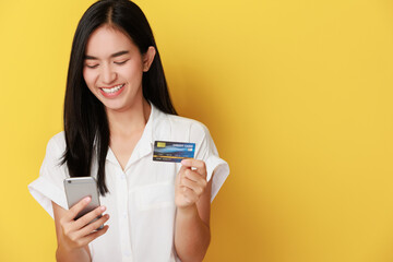Image of excited young lady isolated over yellow background using mobile phone holding credit card.