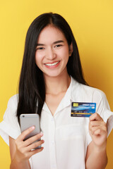 Image of excited young lady isolated over yellow background using mobile phone holding credit card.