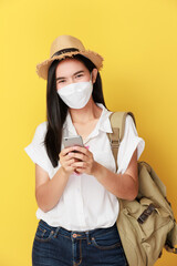 Beautiful travel asian woman with facemask use smart phone isolated on yellow background