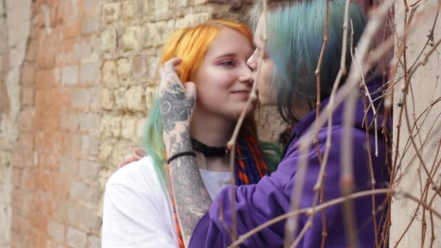 modern young couple guy and girl with colored hair and tattoos hug each other near the wall.