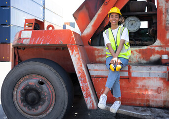Portrait of multiracial woman industrial engineer in hard hat working at logistic container warehouse. Inspector or supervisor in safety vest is responsible for cargo storage and delivery global trade
